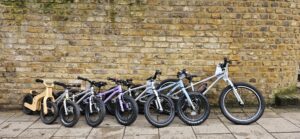 The Early Rider kids bike range lined up against a brick wall outside Butternut Bikes, from a wooden balance bike on the left up to a 24 inch Seeker on the right
