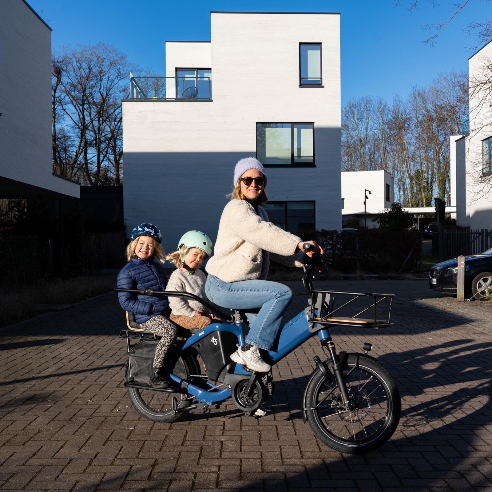 Bike43 Mid in blue with two children on the back, parked on a street