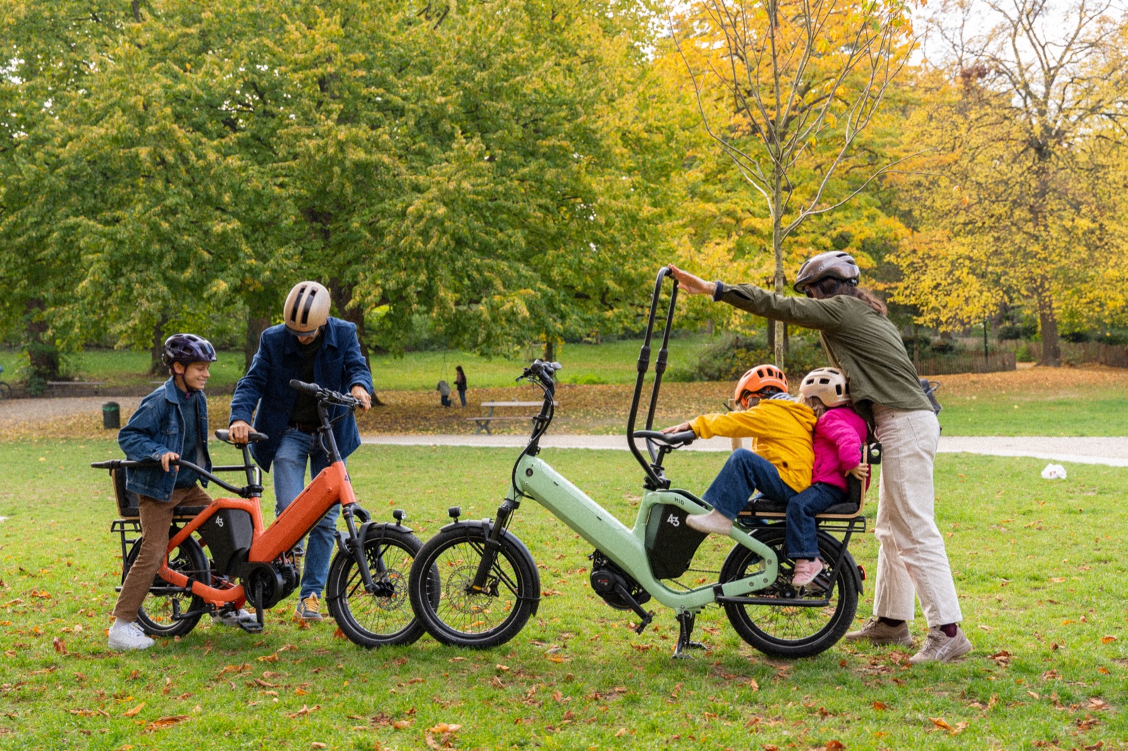 Bike43 Short in orange on the left and Mid in sage on the right, two families in a park