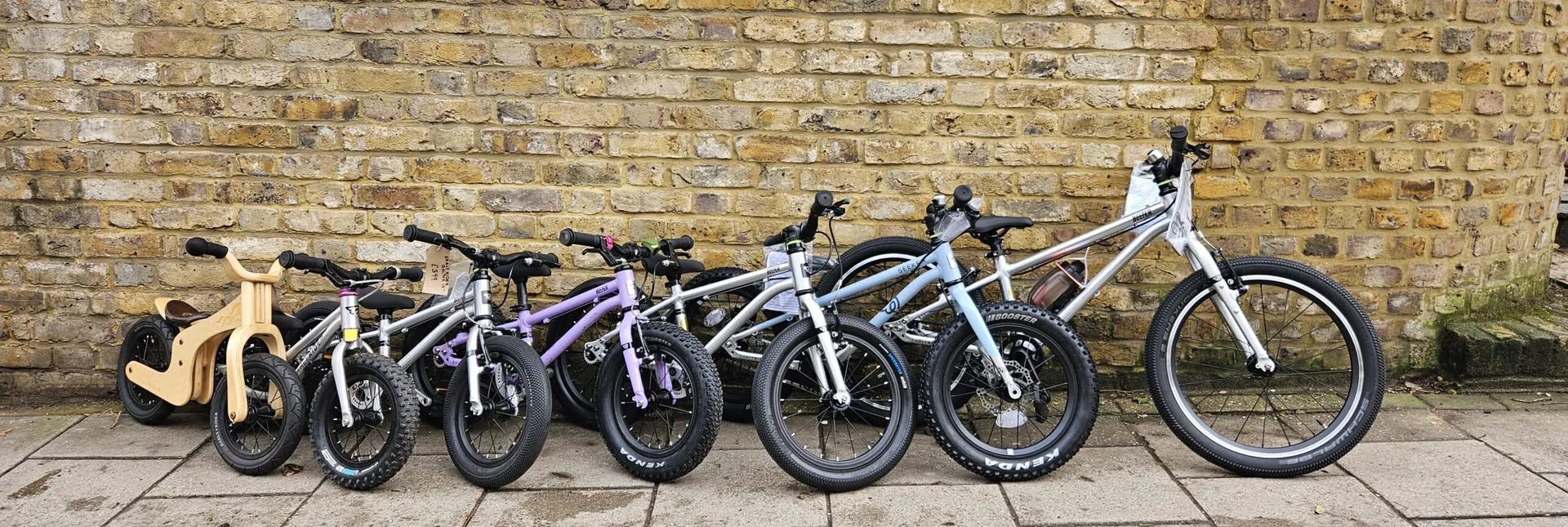 Our Early Rider kids bike range lined up against a brick wall outside Butternut Bikes, from a wooden balance bike up to a 20 inch Belter